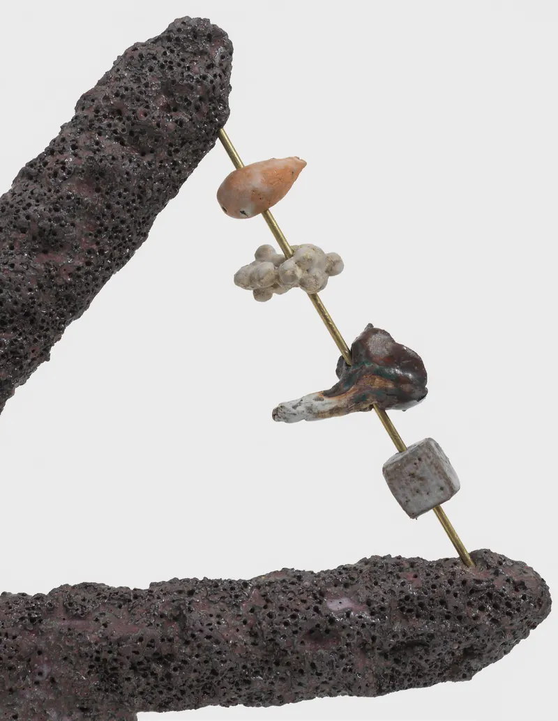 Escultura de Megumi Yuasa: contas cerâmicas atravessadas por uma haste entre duas formas de pedra vulcânica